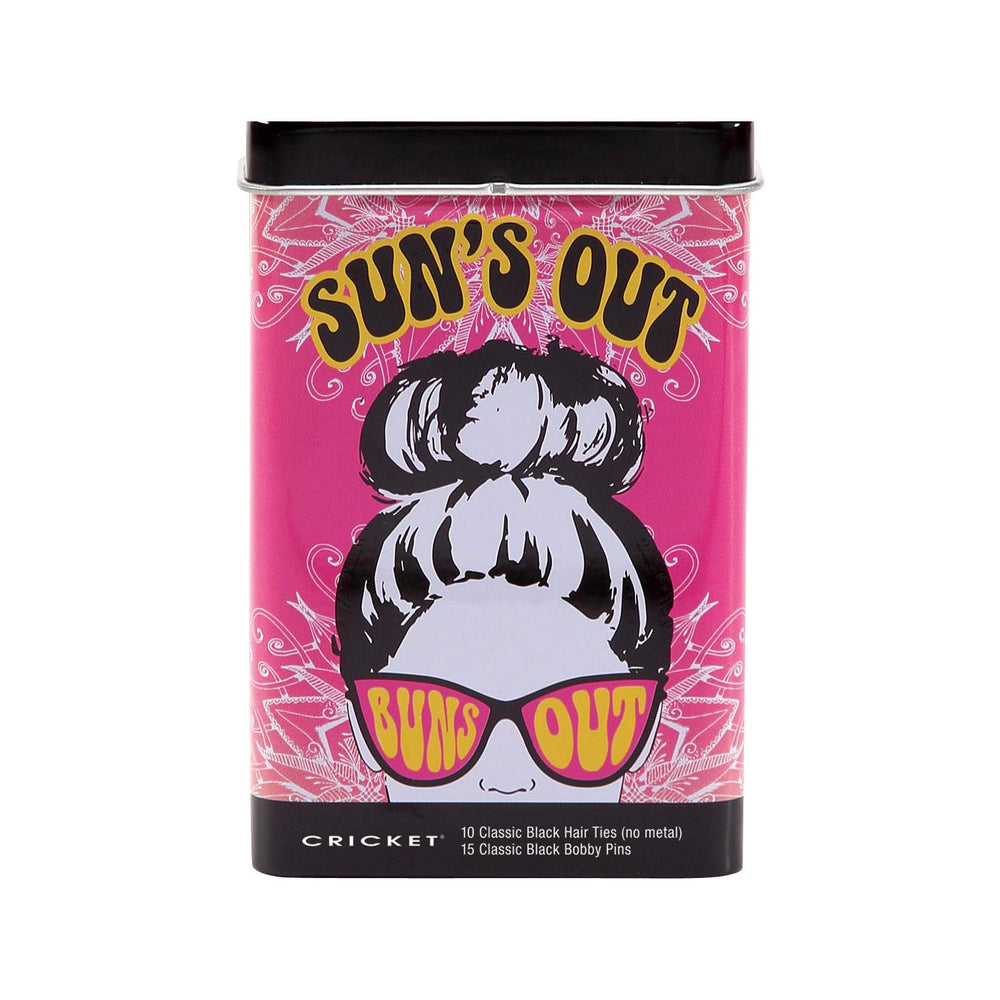 A cylindrical tin of Cricket 'Sun's Out' classic black hair ties and bobby pins on a plain white background. The packaging features a vibrant pink background with a retro illustration of a woman with a high bun wearing pink 'Sun's Out' sunglasses. Cricket logo at the bottom, with the contents of the tin: 10 Classic Black Hair Ties (no metal) and 15 Classic Black bobby pins.
