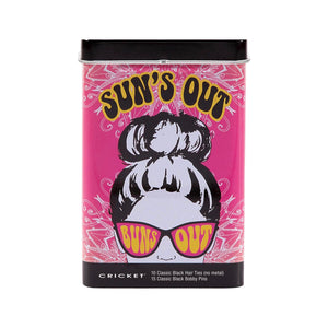 A cylindrical tin of Cricket 'Sun's Out' classic black hair ties and bobby pins on a plain white background. The packaging features a vibrant pink background with a retro illustration of a woman with a high bun wearing pink 'Sun's Out' sunglasses. Cricket logo at the bottom, with the contents of the tin: 10 Classic Black Hair Ties (no metal) and 15 Classic Black bobby pins.