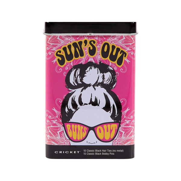 A cylindrical tin of Cricket 'Sun's Out' classic black hair ties and bobby pins on a plain white background. The packaging features a vibrant pink background with a retro illustration of a woman with a high bun wearing pink 'Sun's Out' sunglasses. Cricket logo at the bottom, with the contents of the tin: 10 Classic Black Hair Ties (no metal) and 15 Classic Black bobby pins.
